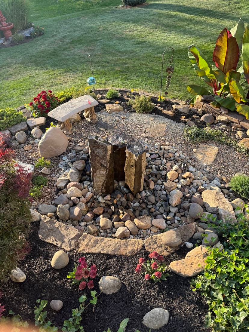 Stone fire pit surrounded by colorful flowers and lush green grass in a serene garden setting.