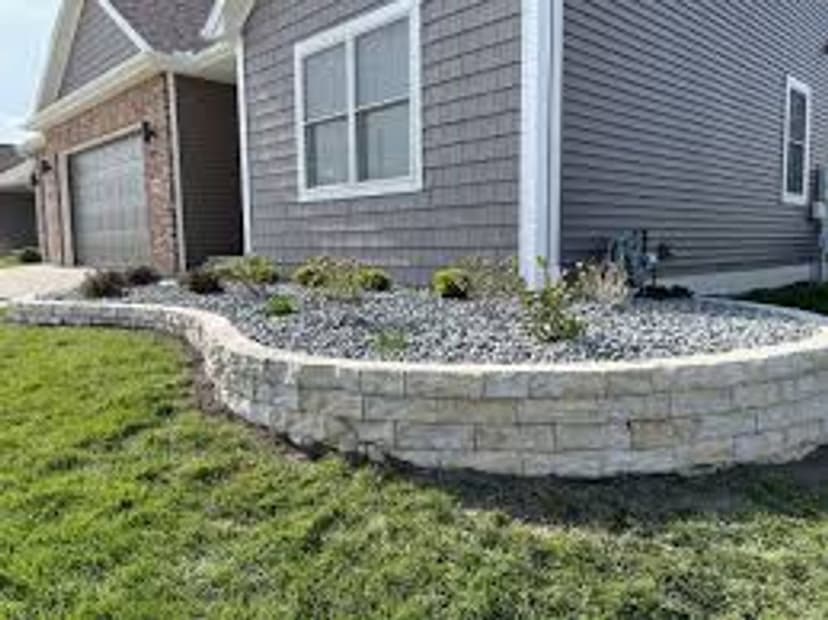 Stone landscape border with gravel and plants near a modern home exterior.